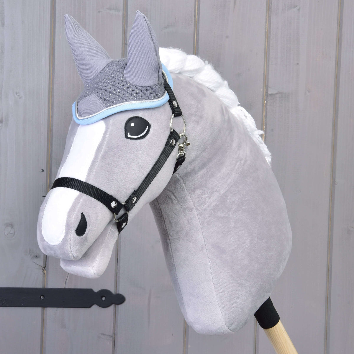Grey Hobby Horse with a white braided mane and black halter wearing the Ear bonnet crocheted grey with light blue trim