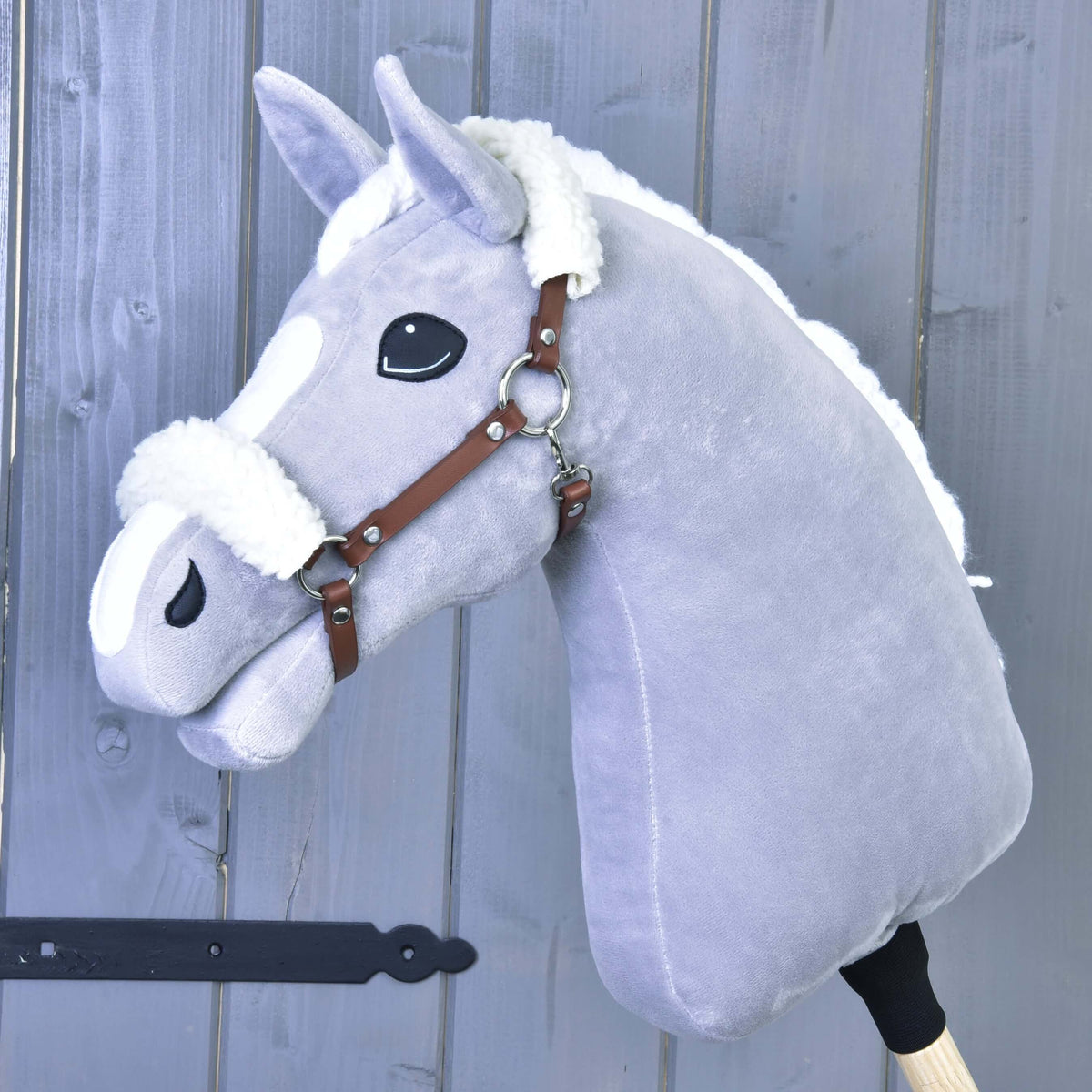 Siv Hobby Horse konj z belo grivo nosi konjak rjavo oglavko z belim krznom na zatilnem jermenu in sprednjem delu nosnika
