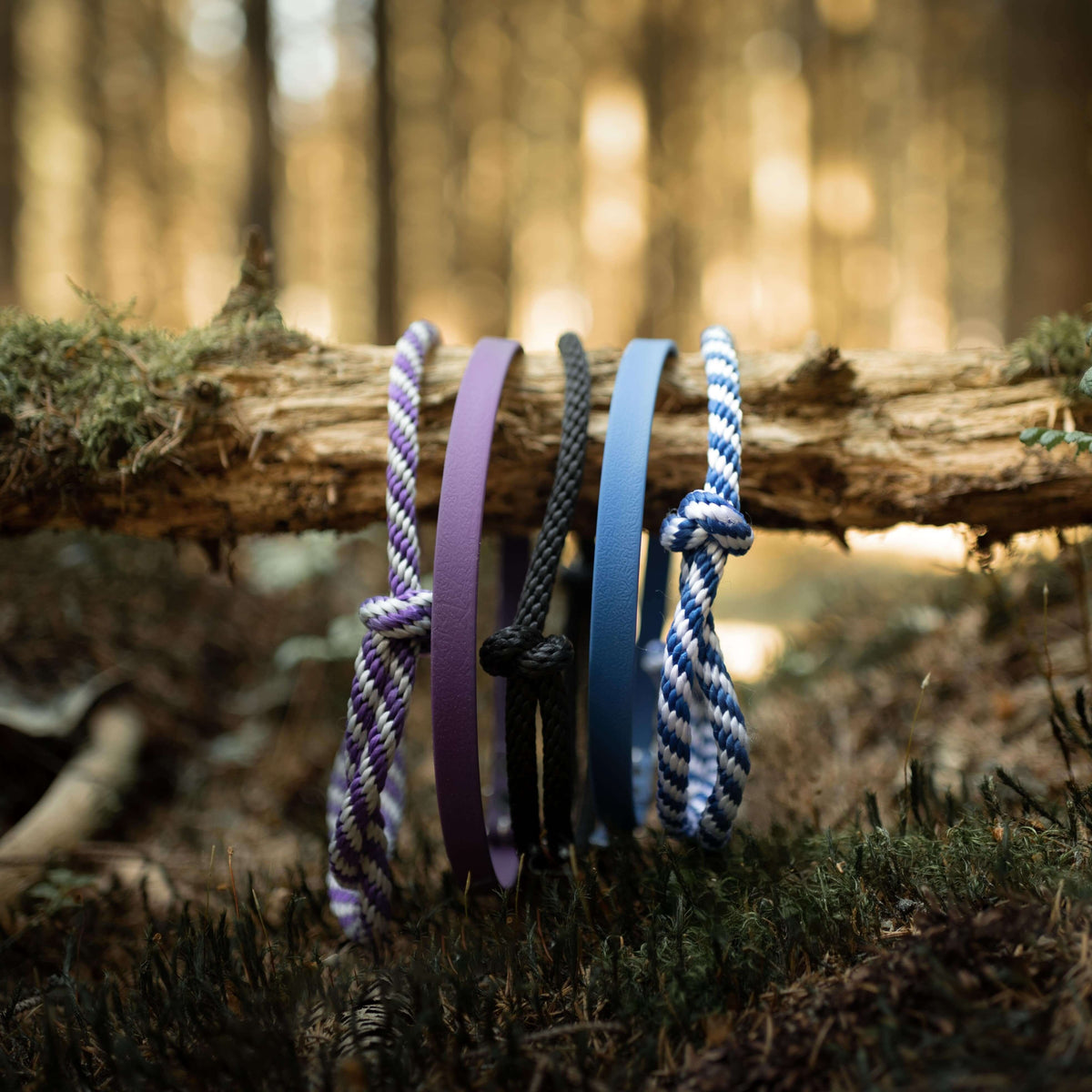 Five Hobby Horse cordeos in purple, black and blue rope and leatherette hanging over a mossy log in the forest