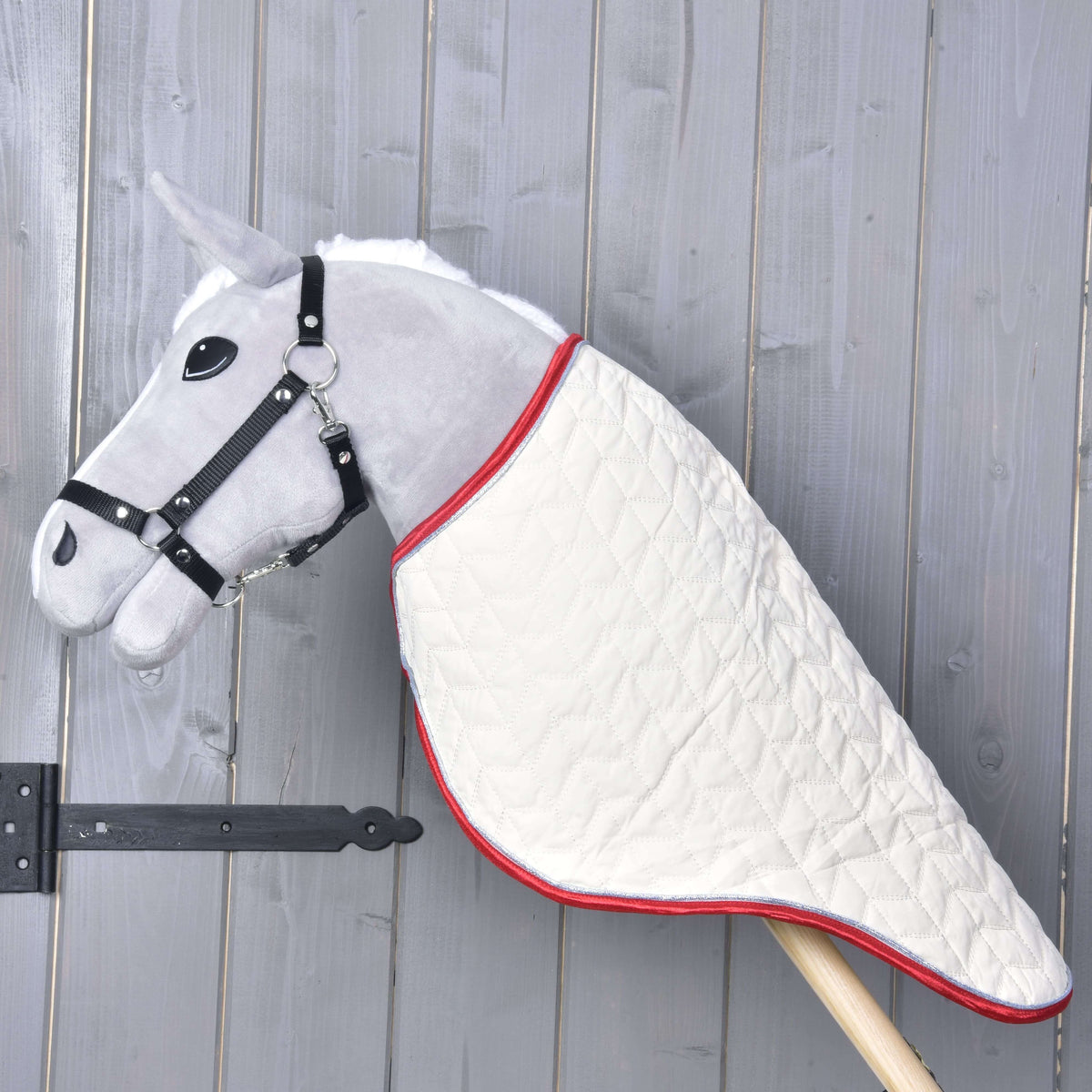 Siv Hobby Horse konj v profilu s kremnim prešitim transportnim pregrinjalom, ki pokriva vrat do lesene palice