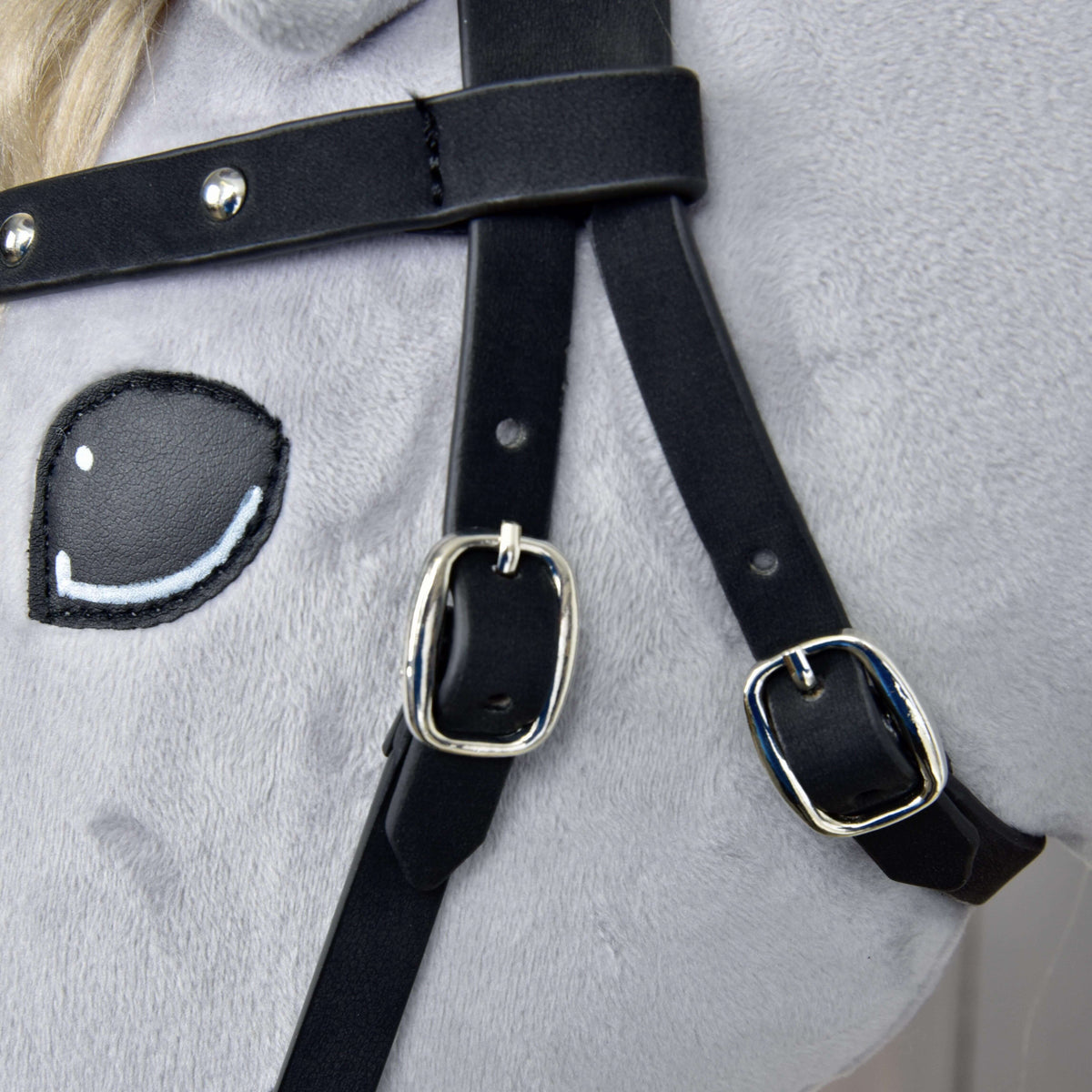 Close-up of two silver buckles on the black cheekpieces below the studded browband, next to the stitched eye