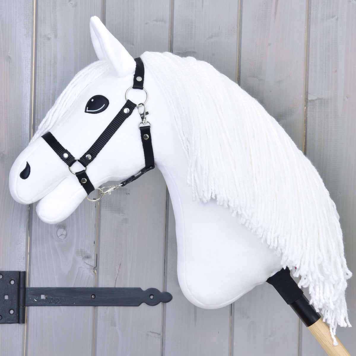 Pogled od strani na belega Hobby Horse konja z dolgo belo grivo iz preje in črno najlonsko oglavko na leseni palici