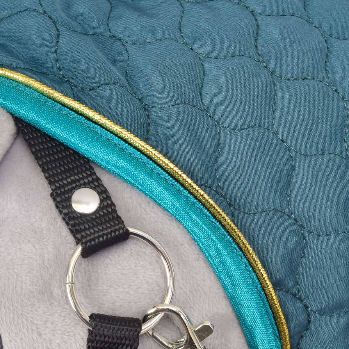 Close-up of the Lagoon neck edge with turquoise binding and gold piping beside a black halter strap and silver ring