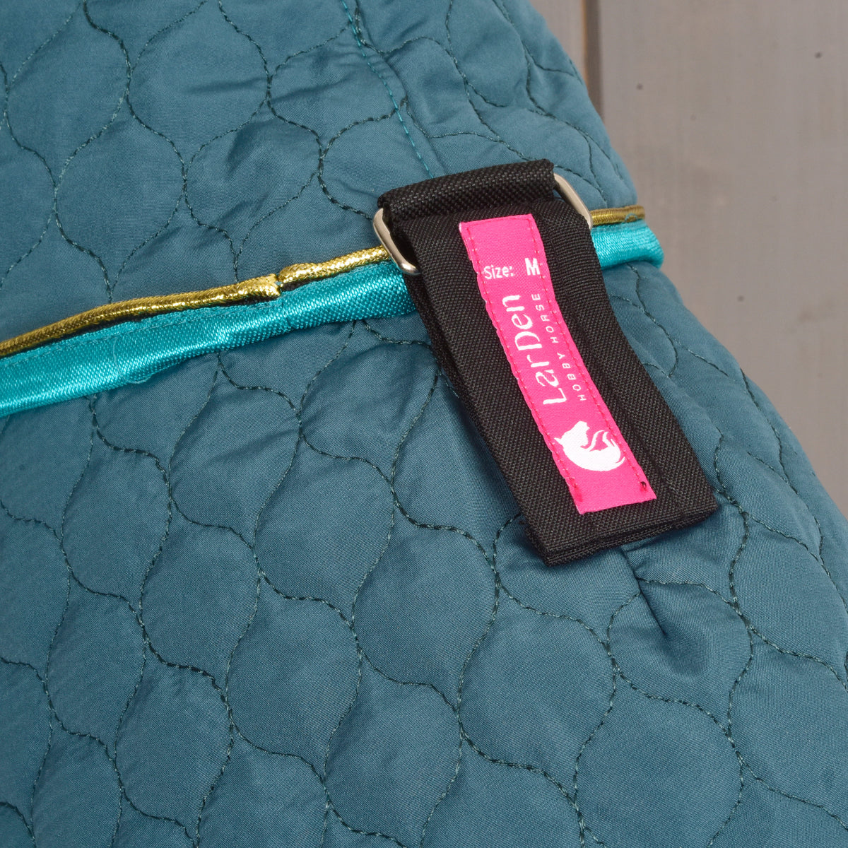 Close-up of a pink LarDen label on a black strap of the Lagoon blanket, above the turquoise binding and gold piping