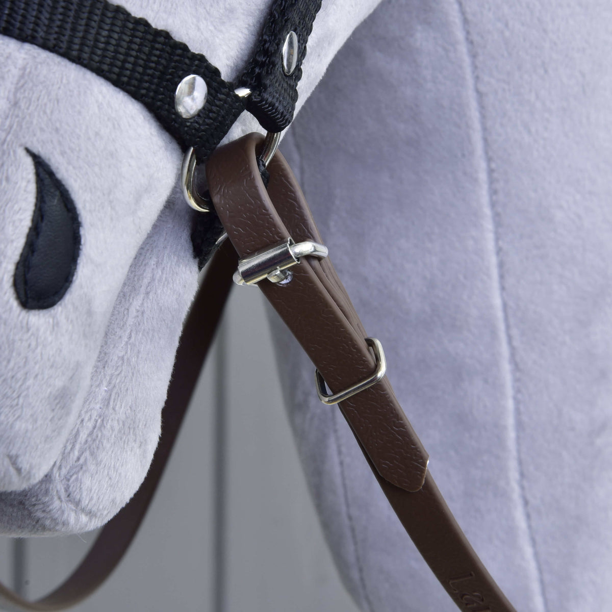Bližnji posnetek rjave zaponke vajeti, vodila in zanke, zapetih na obroček oglavke pod brado sivega Hobby Horse konja