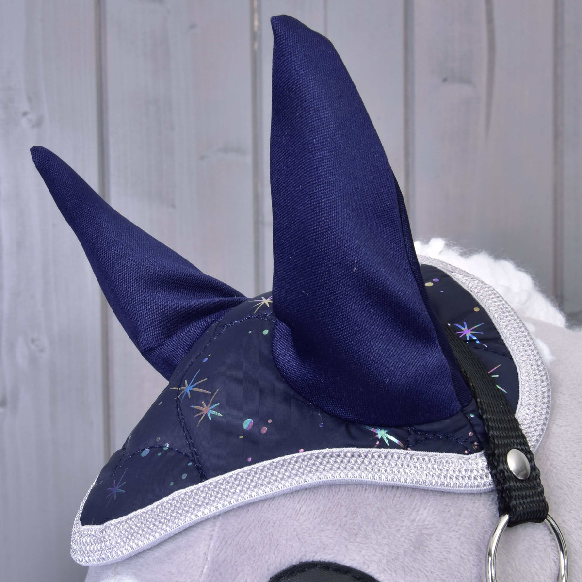 Close-up of the Set Magic ear bonnet with tall navy ears, holographic star print and braided grey edging