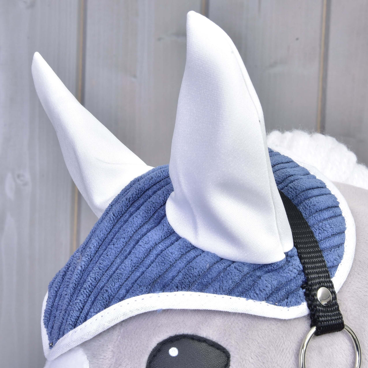 Close-up of the Set Manchester Plum ear bonnet in blue corduroy with white ears and trim on a grey Hobby Horse