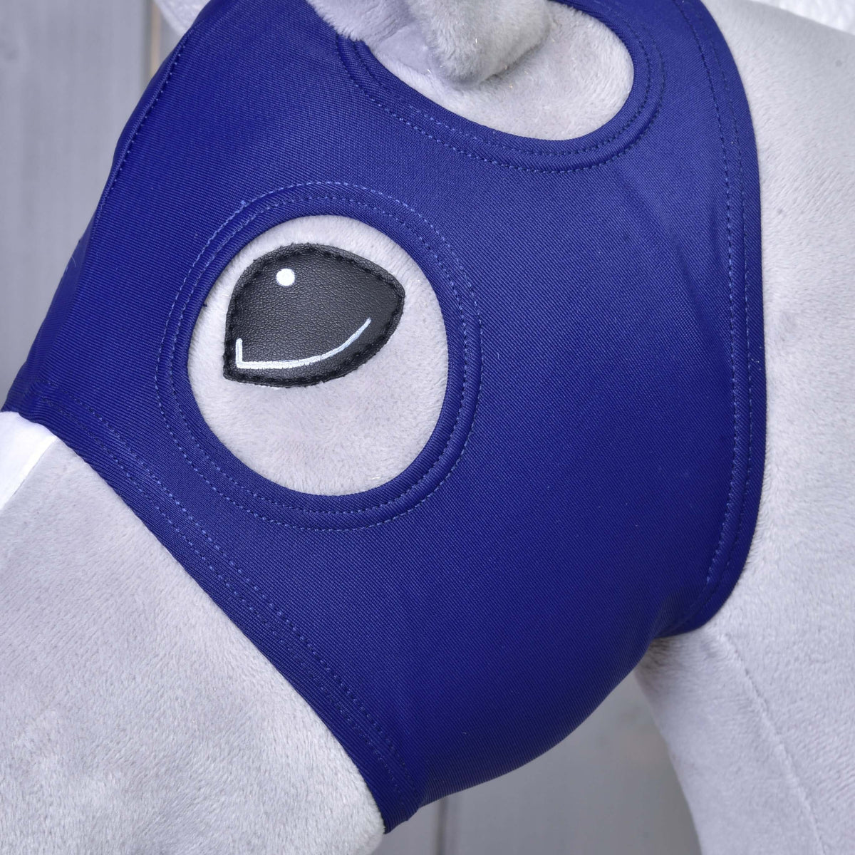 Bližnji posnetek maske brez ušes na Hobby Horse konju: temno modro blago obkroža črno oko, nad njim je odprtina za uho