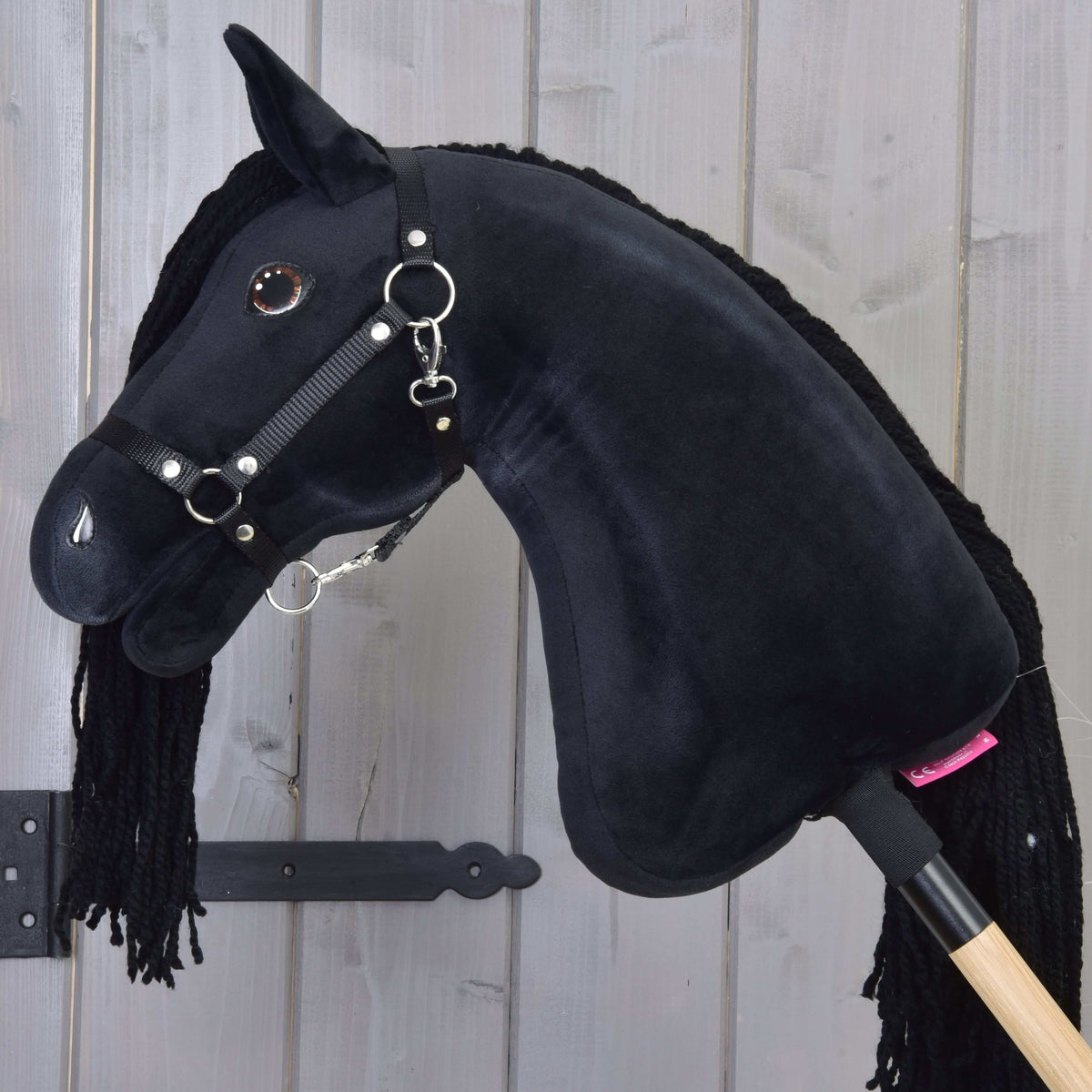 Side view of the black Hobby Horse with the mane on the far side, a black nylon halter and wooden stick