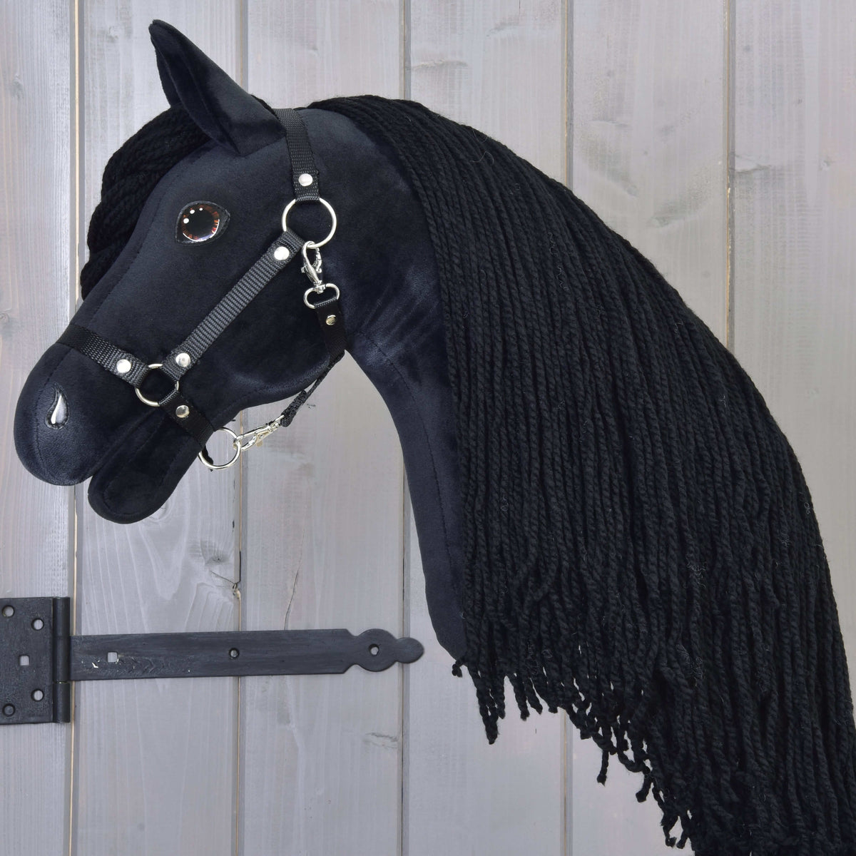 Black Hobby Horse in profile with a long black yarn mane over the neck and a black halter with silver rings