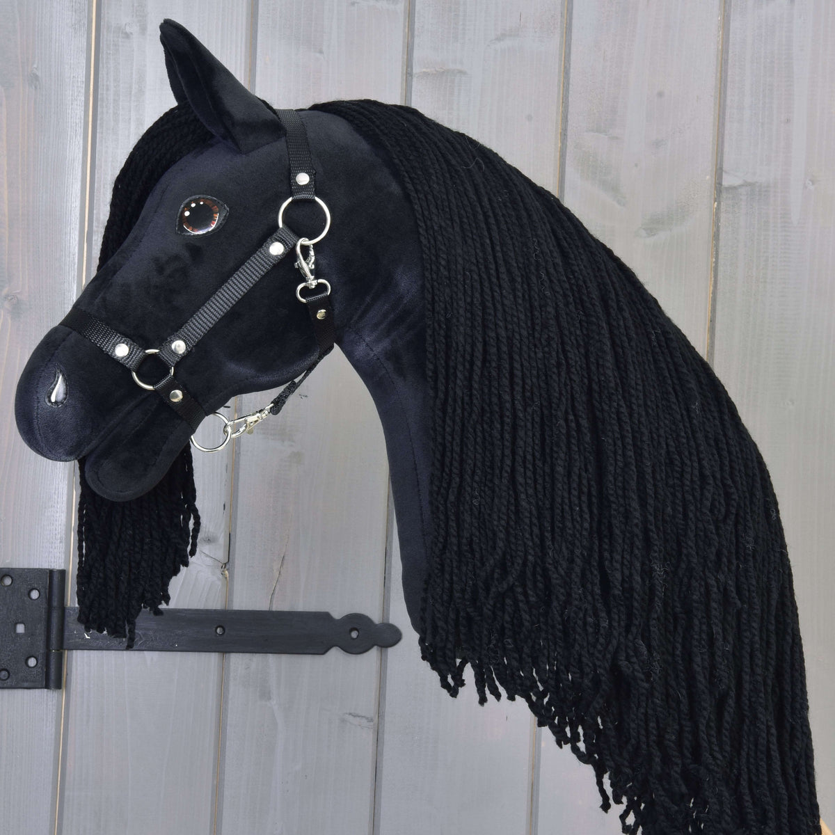 Close side view of the black plush head with a glossy brown eye, black halter and very long black yarn mane