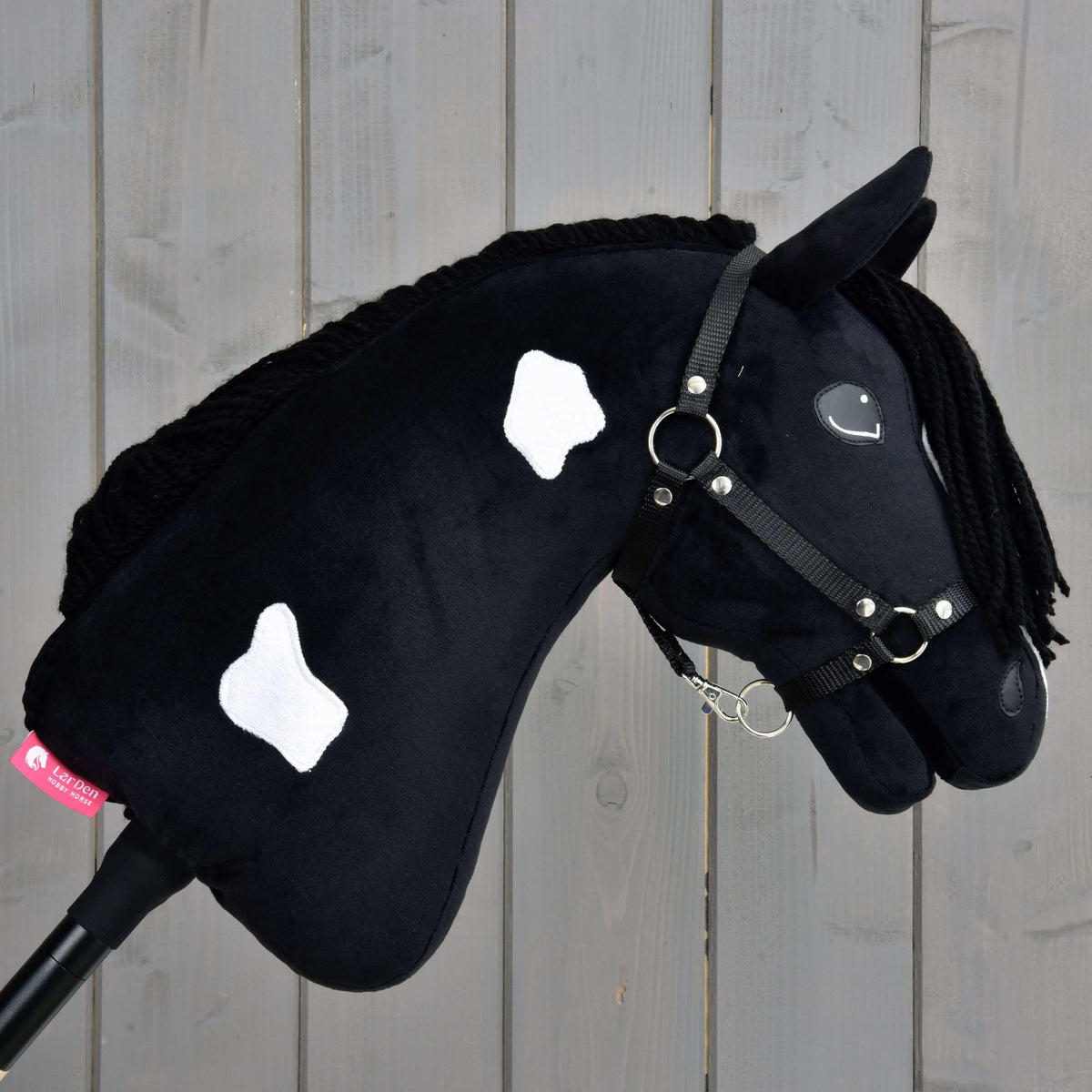Hobby Horse Merlin with Black Halter facing right, small white patches on the black neck and a pink LarDen label