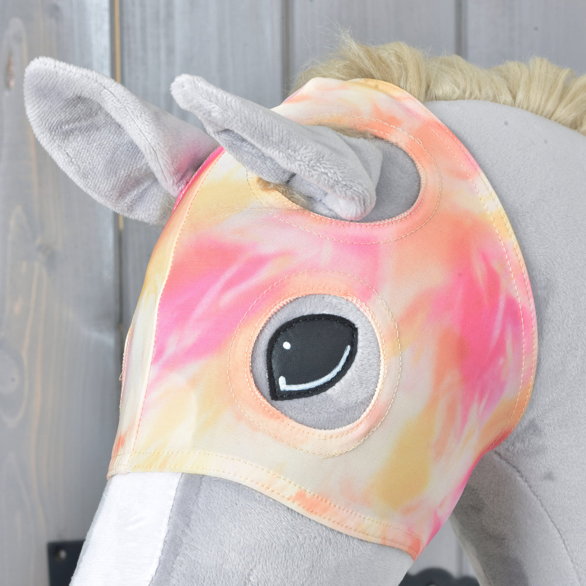Bližnji posnetek maske Mirage na sivem Hobby Horse konju: plišasta ušesa gledajo skozi odprtini, robovi okoli odprtine za oko so obšiti
