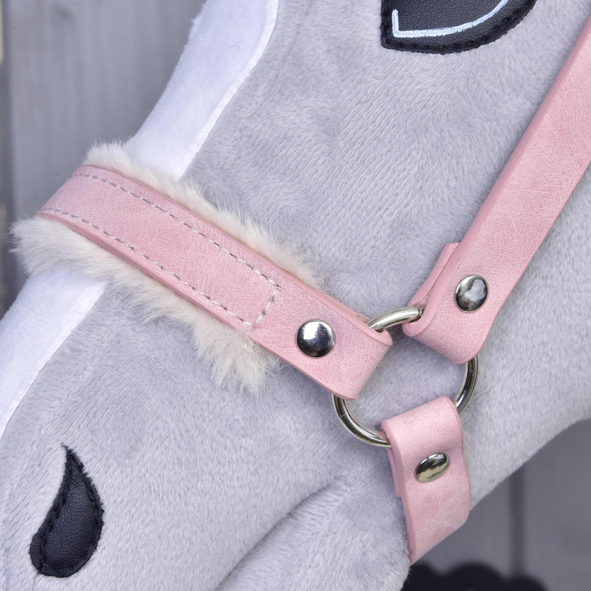 Close-up of the dusty pink noseband with cream fur, fine stitching and a silver ring on a grey Hobby Horse