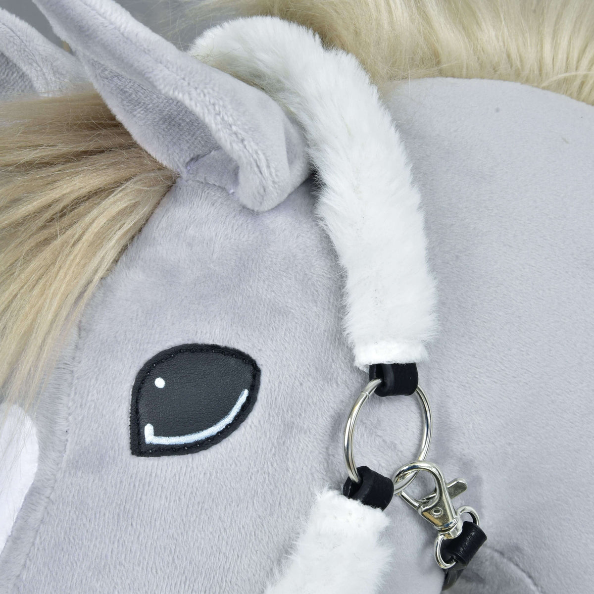 Close-up of the white fur crownpiece behind the ear with a silver ring, snap hook and black leatherette tabs