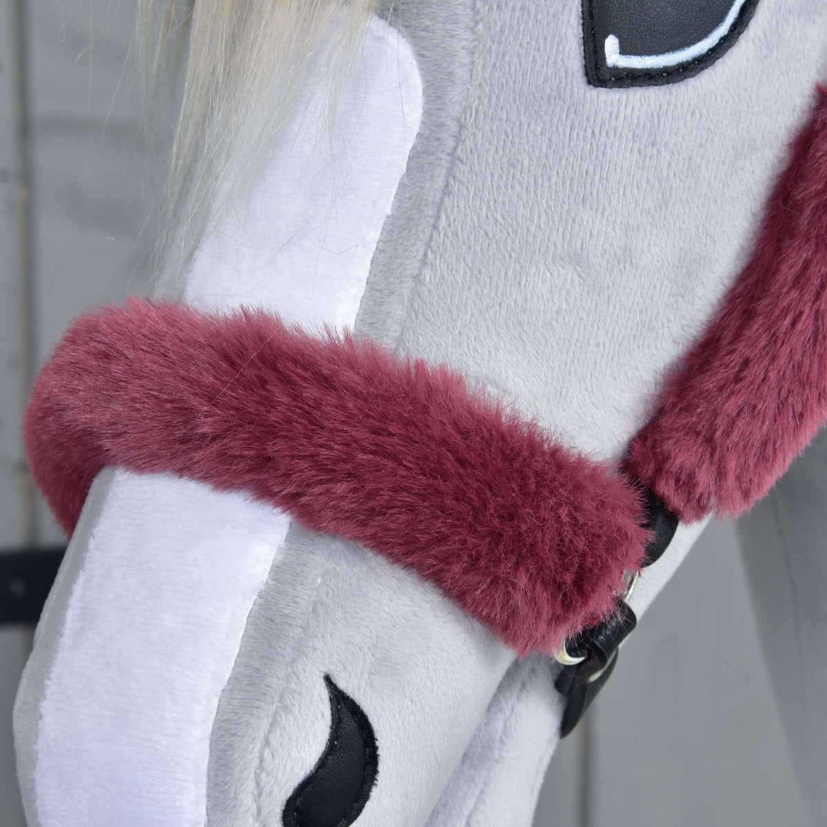 Close-up of the fluffy maroon fur noseband resting over the white blaze and stitched nostril of a grey plush head