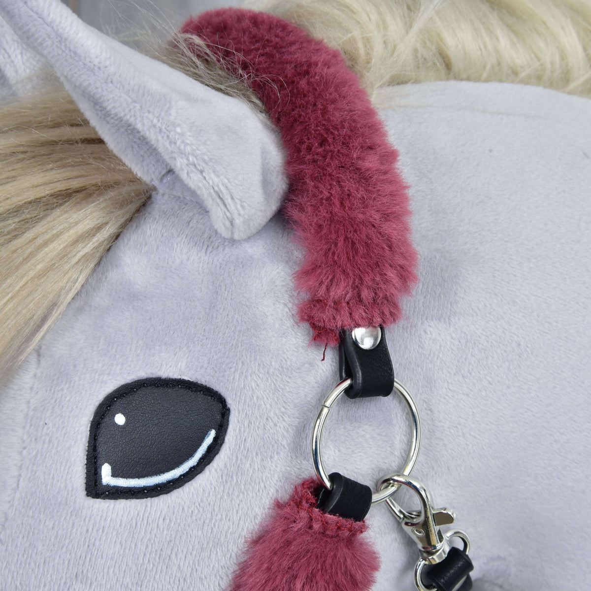 Close-up of the maroon fur crownpiece behind the ear, ending in a black leatherette tab with a silver ring