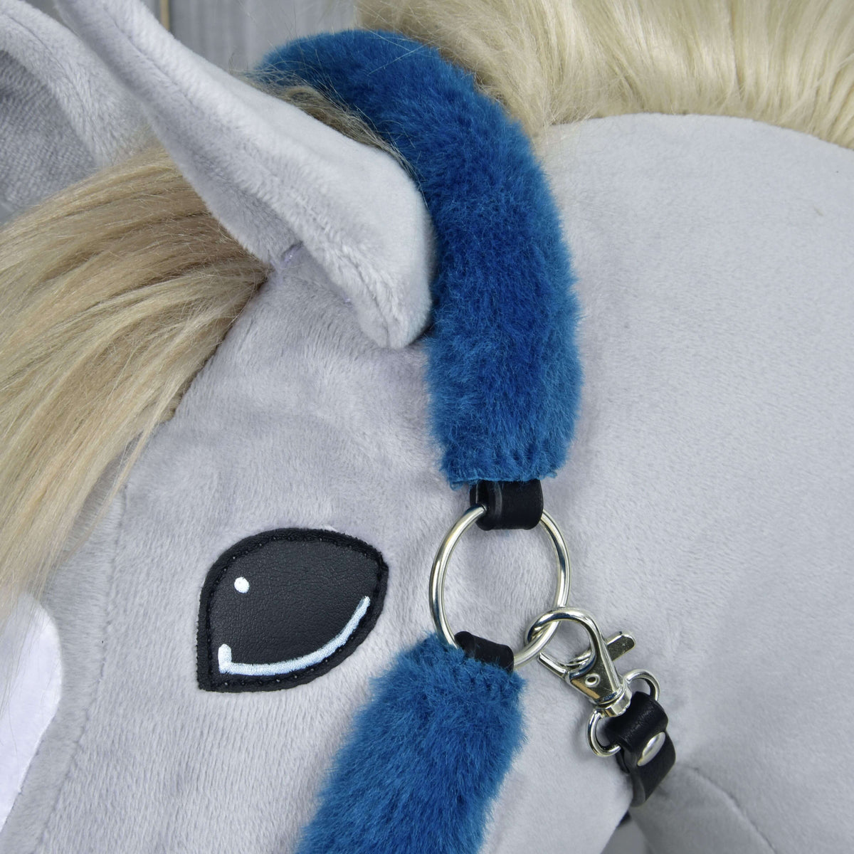 Close-up of the petrol blue fur crownpiece behind the ear, with a silver ring, snap hook and black leatherette tabs