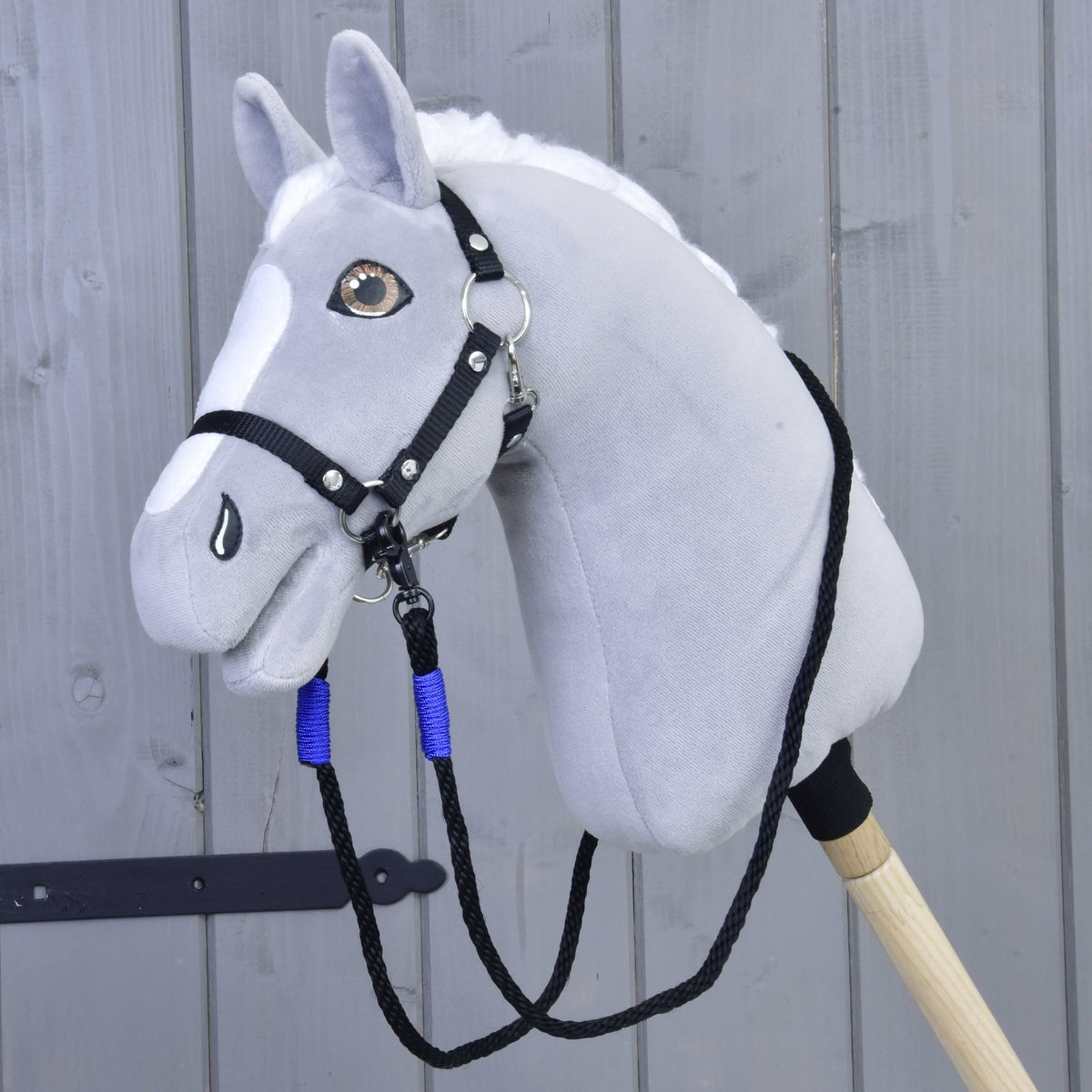 Siv plišast Hobby Horse konj s črno oglavko in črnimi vrvičnimi vajetmi z modrimi ovoji, pripetimi pod brado