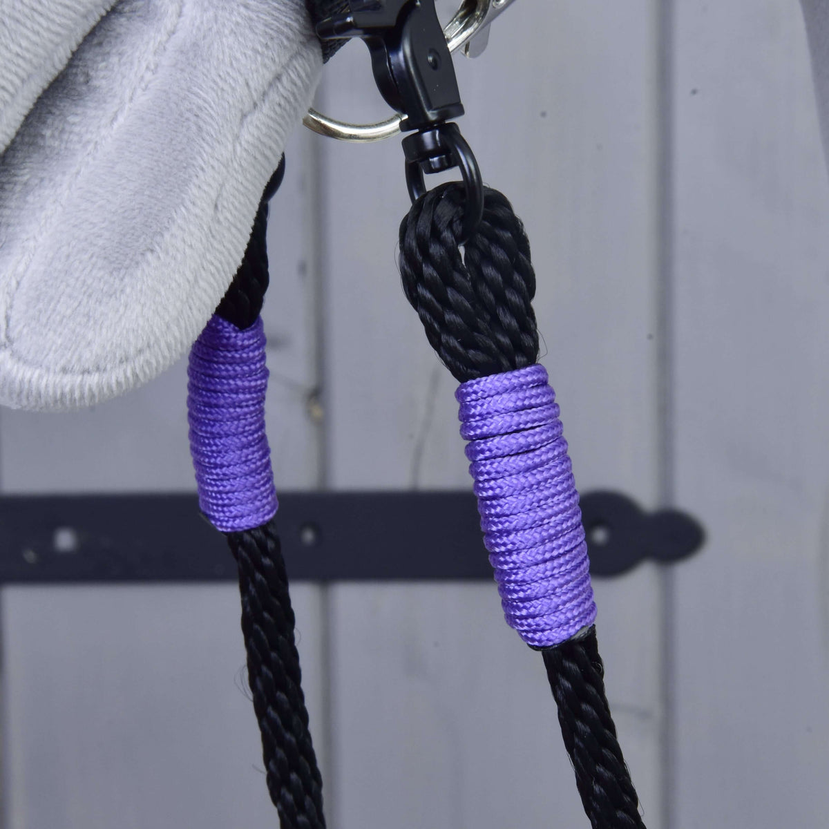 Close-up of the lilac thread wraps and black swivel snap on the braided reins below a grey plush muzzle