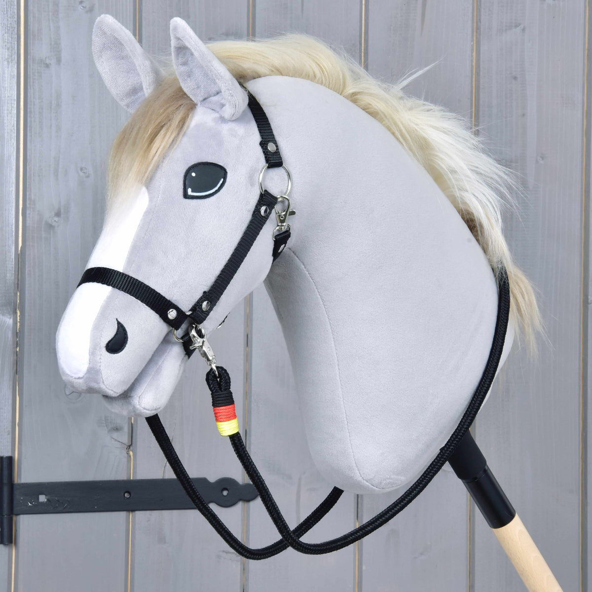 Grey Hobby Horse in a black halter with Reins Emblem clipped on, the black rope reins hanging down to the stick