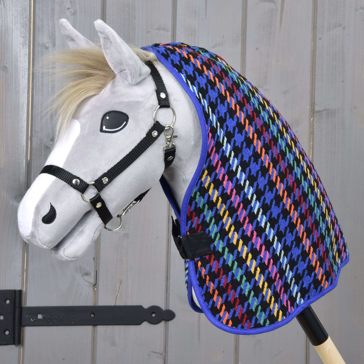 Siv Hobby Horse konj z blond grivo in črno oglavko nosi čez vrat živobarvno hlevsko pregrinjalo Peru v vzorcu pepita