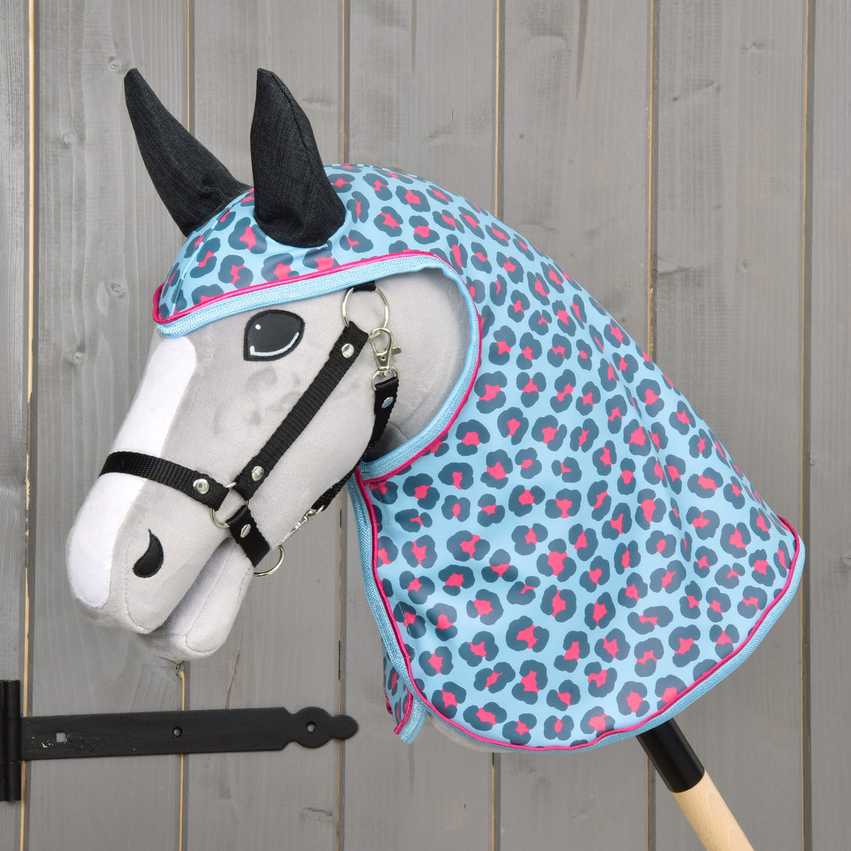 Svetlo siv Hobby Horse konj s črno oglavko nosi dežno pregrinjalo Blue Leopard s temnimi ušesi in svetlo modro obrobo z roza robom