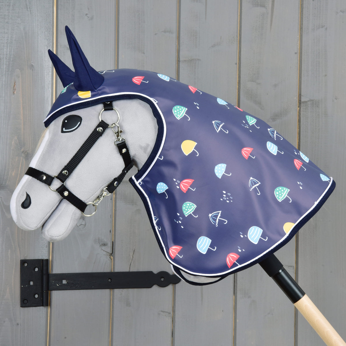 Side view of a grey Hobby Horse in the umbrella print raincoat, the hood covering head and neck down to the stick