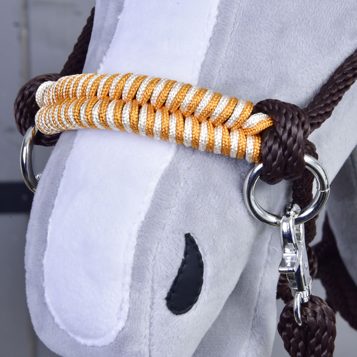 Detajl oranžno-belega pletenega nosnika in rjavega vrvičnega vozla oranžnega Hobby Horse vrvičnega kompleta na sivi glavi