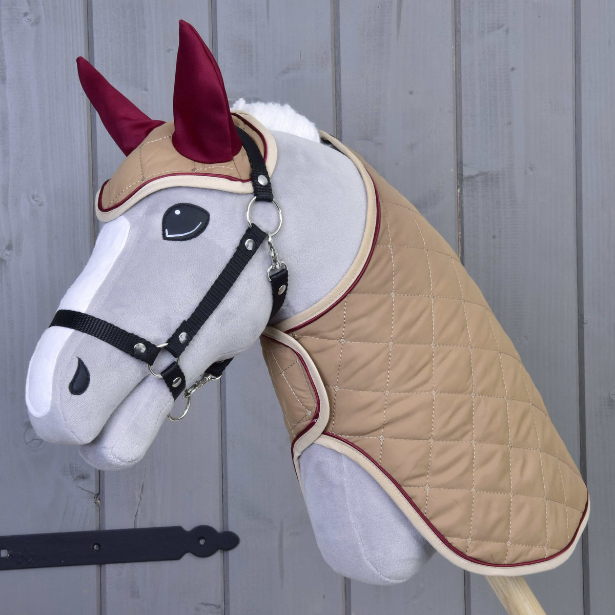 Siv Hobby Horse konj s črno oglavko, oblečen v bež prešito pregrinjalo in naušnike z bordo ušesi