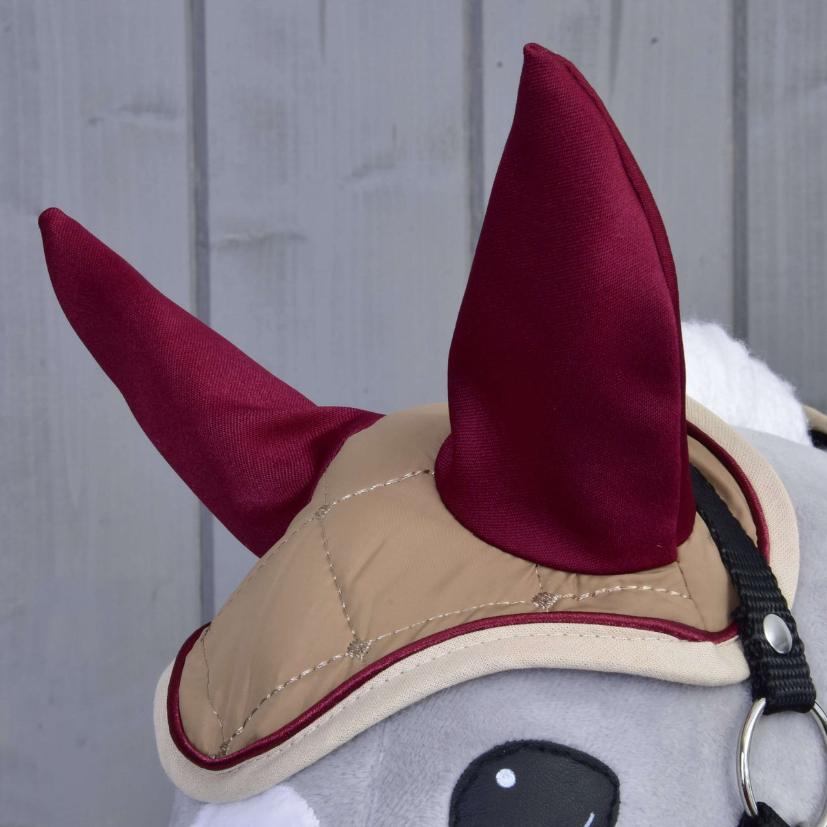 Bližnji posnetek bež prešitih naušnikov z bordo ušesi, bordo paspulom in kremno obrobo na Hobby Horse konju