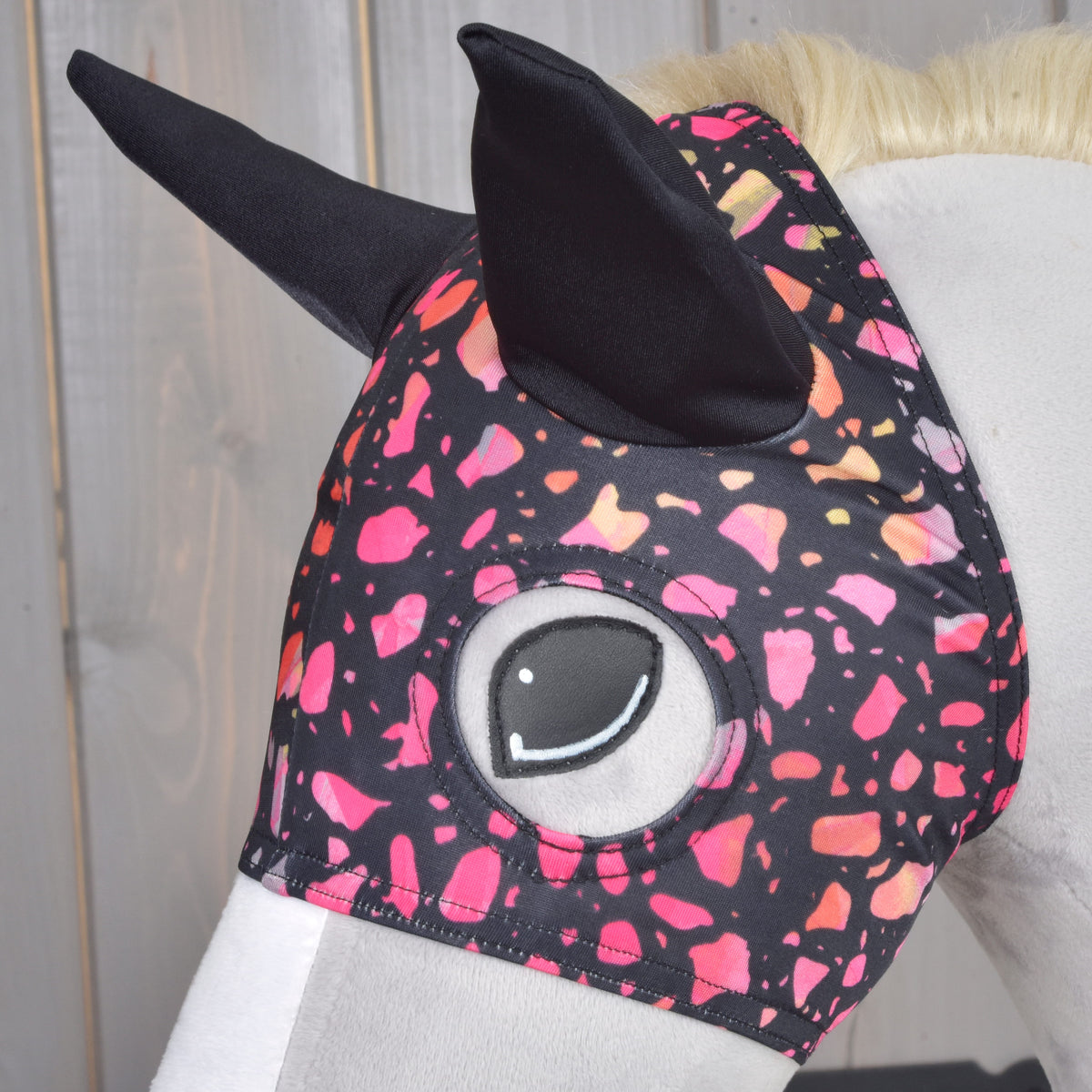 Bližnji posnetek maske Roxy na sivem Hobby Horse konju: črna ušesa in odprtina za oko, obdana z roza in koralnim pikčastim potiskom