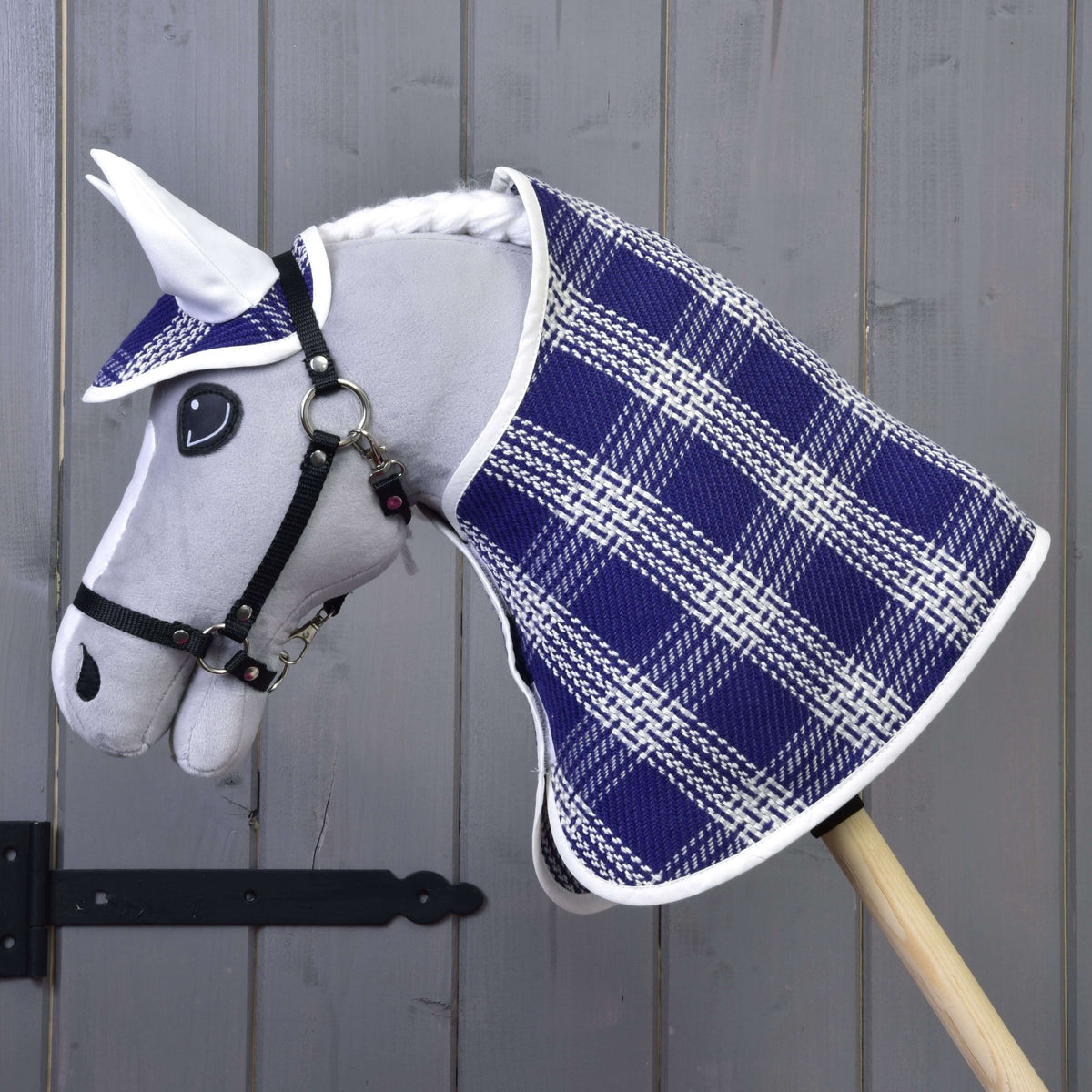 Pogled od strani na sivega Hobby Horse konja v modro-belem karirastem pregrinjalu in naušnikih z belimi ušesnimi deli
