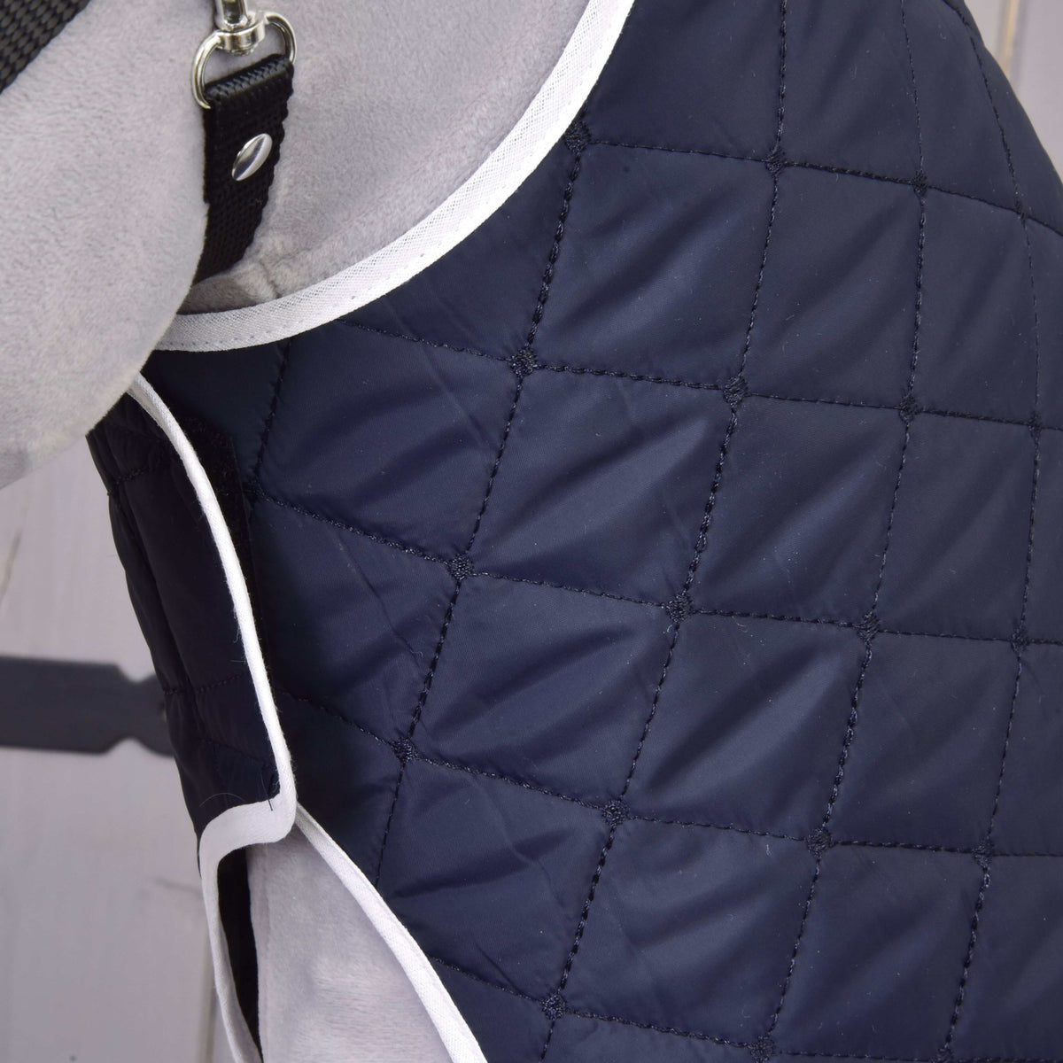 Close-up of the navy diamond quilting and white binding at the front of the Set Monte blanket on a grey Hobby Horse
