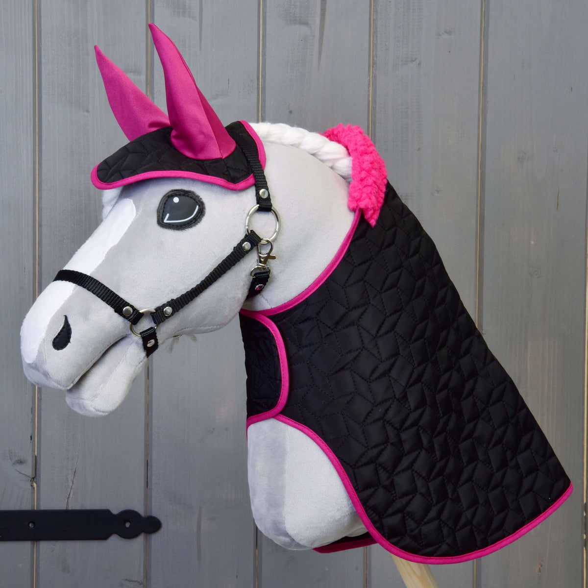 Siv Hobby Horse konj v črni oglavki nosi prešito črno pregrinjalo z roza krznenim ovratnikom in naušnike z roza ušesnimi deli