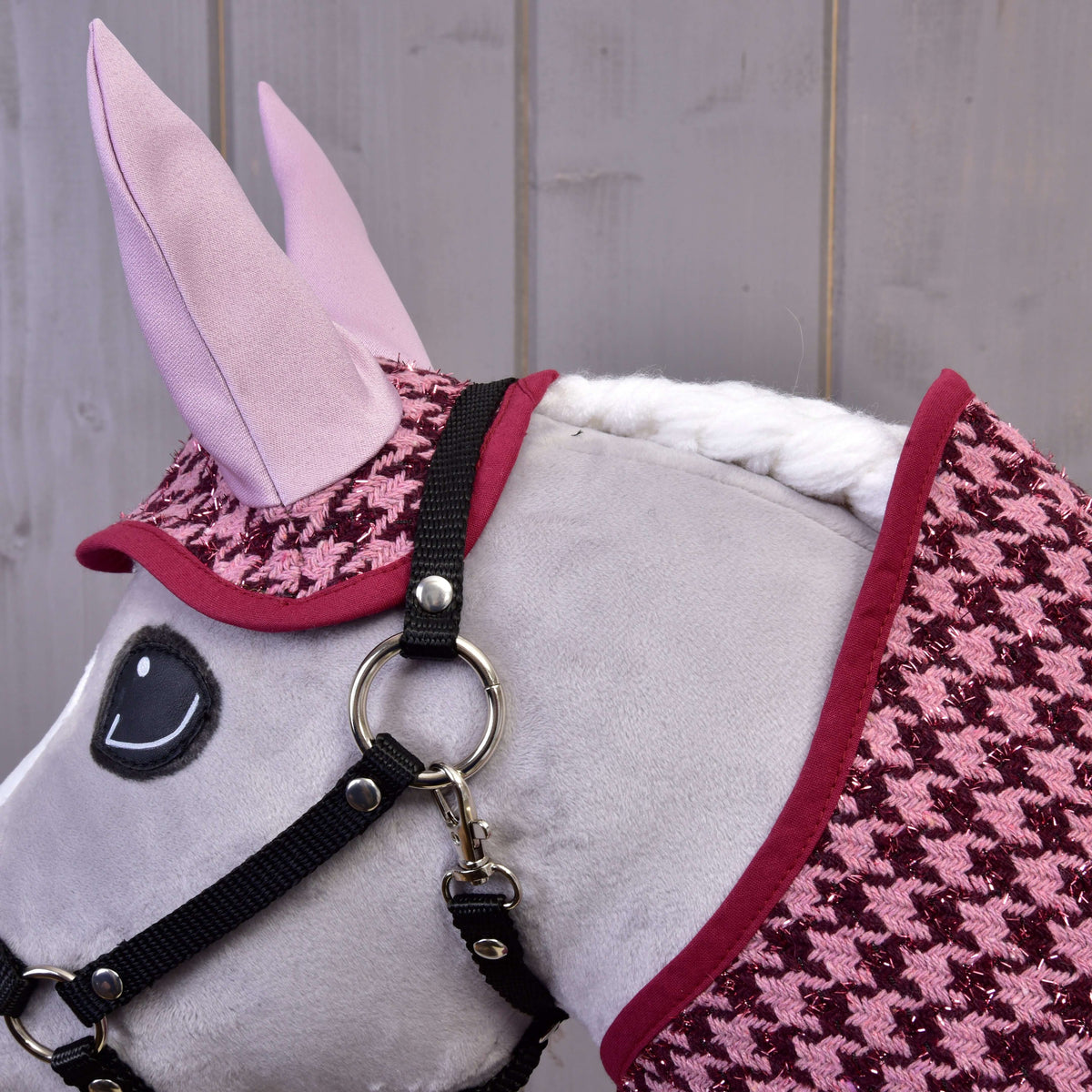 Close-up of the houndstooth ear bonnet with light pink ears and the blanket's burgundy binding on a grey Hobby Horse