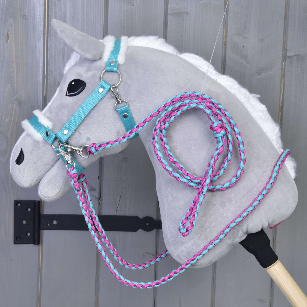 Svetlo siv Hobby Horse konj s turkizno oglavko z belim krznom ter pletenimi vajetmi in povodcem v roza in turkizni barvi