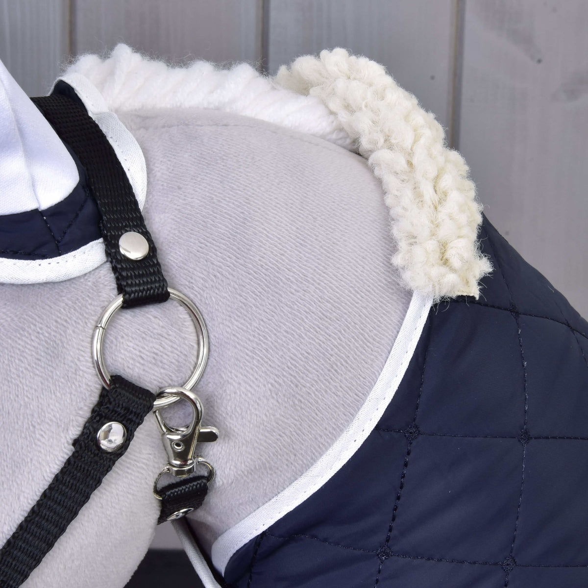 Bližnji posnetek kremnega ovratnika iz flisa in temno modrega prešitega pregrinjala z belo obrobo na plečih sivega Hobby Horse konja