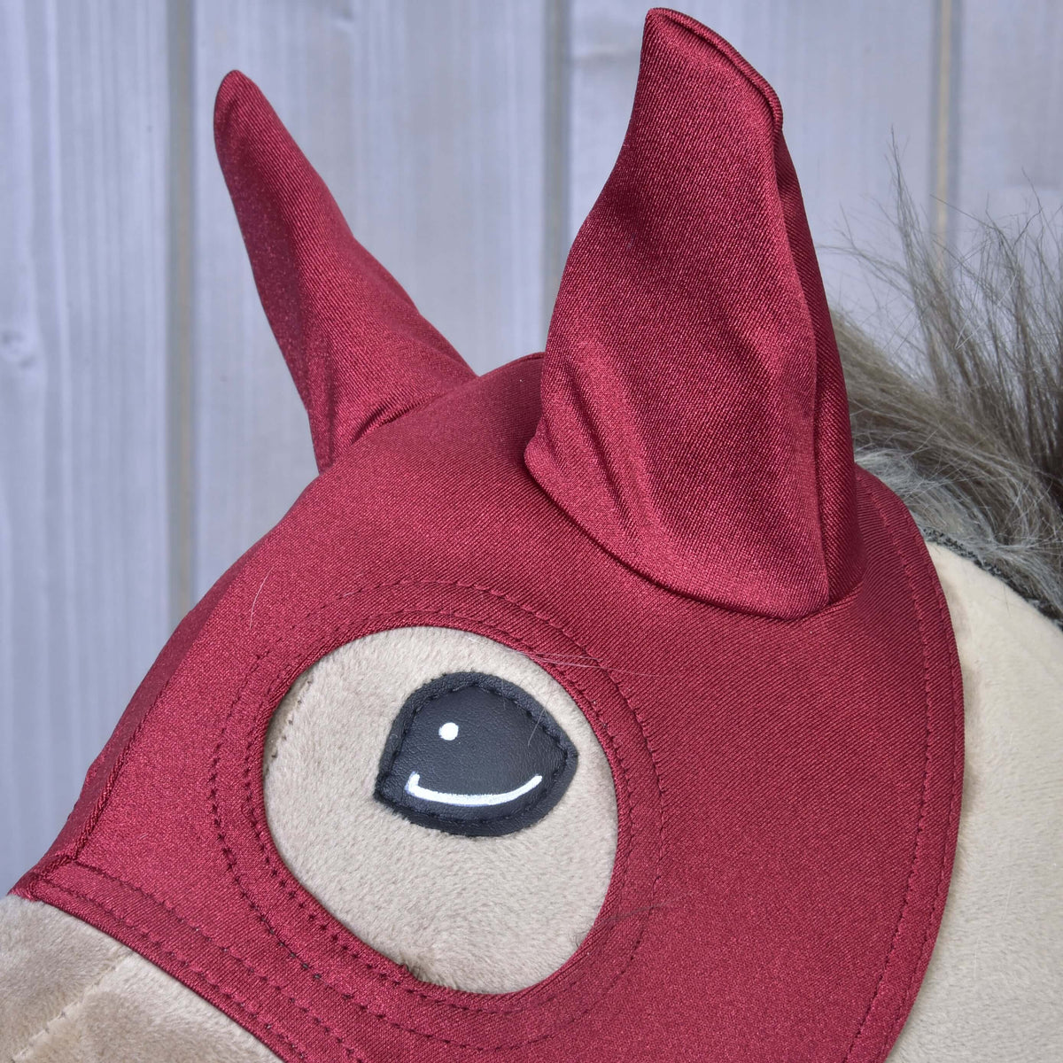 Detajl svetlečih temno rdečih ušesnih delov maske Barn Red z obšito odprtino za oko spodaj, na bež Hobby Horse konju