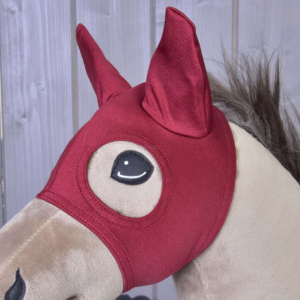 Bližnji posnetek temno rdeče maske Barn Red na bež Hobby Horse konju, obe ušesi v koničastih ušesnih delih in oko, obrobljeno s šivom