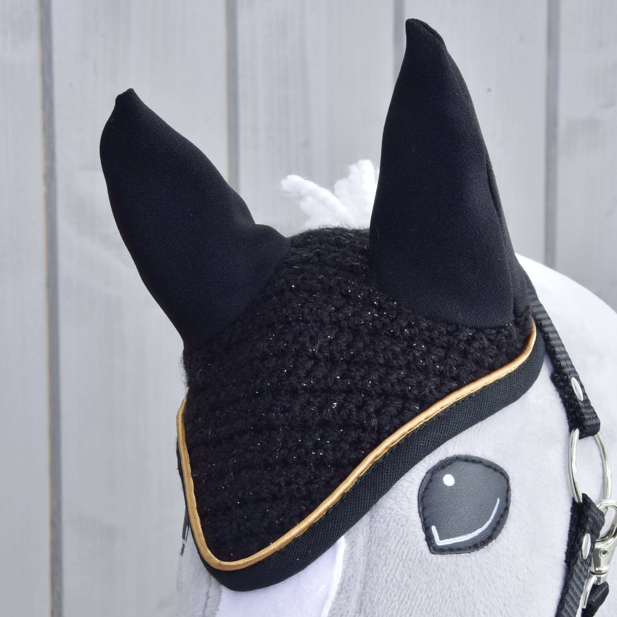 Close-up of the crocheted black ear bonnet with sparkling yarn, black fabric ears and gold piping on a grey head