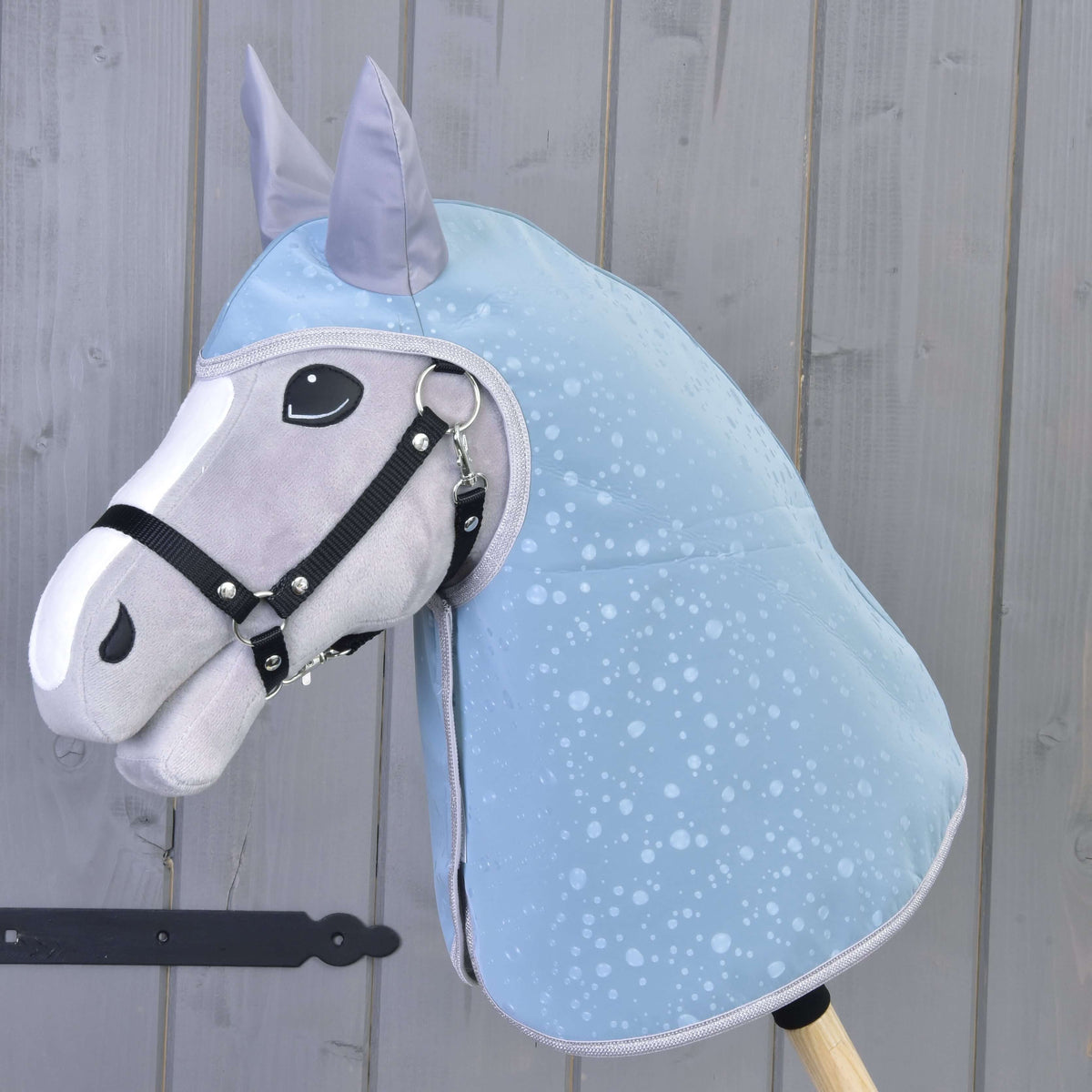 Raincoat Blue Drops on a grey Hobby Horse with white blaze and black halter, covering head and neck, by a grey plank wall