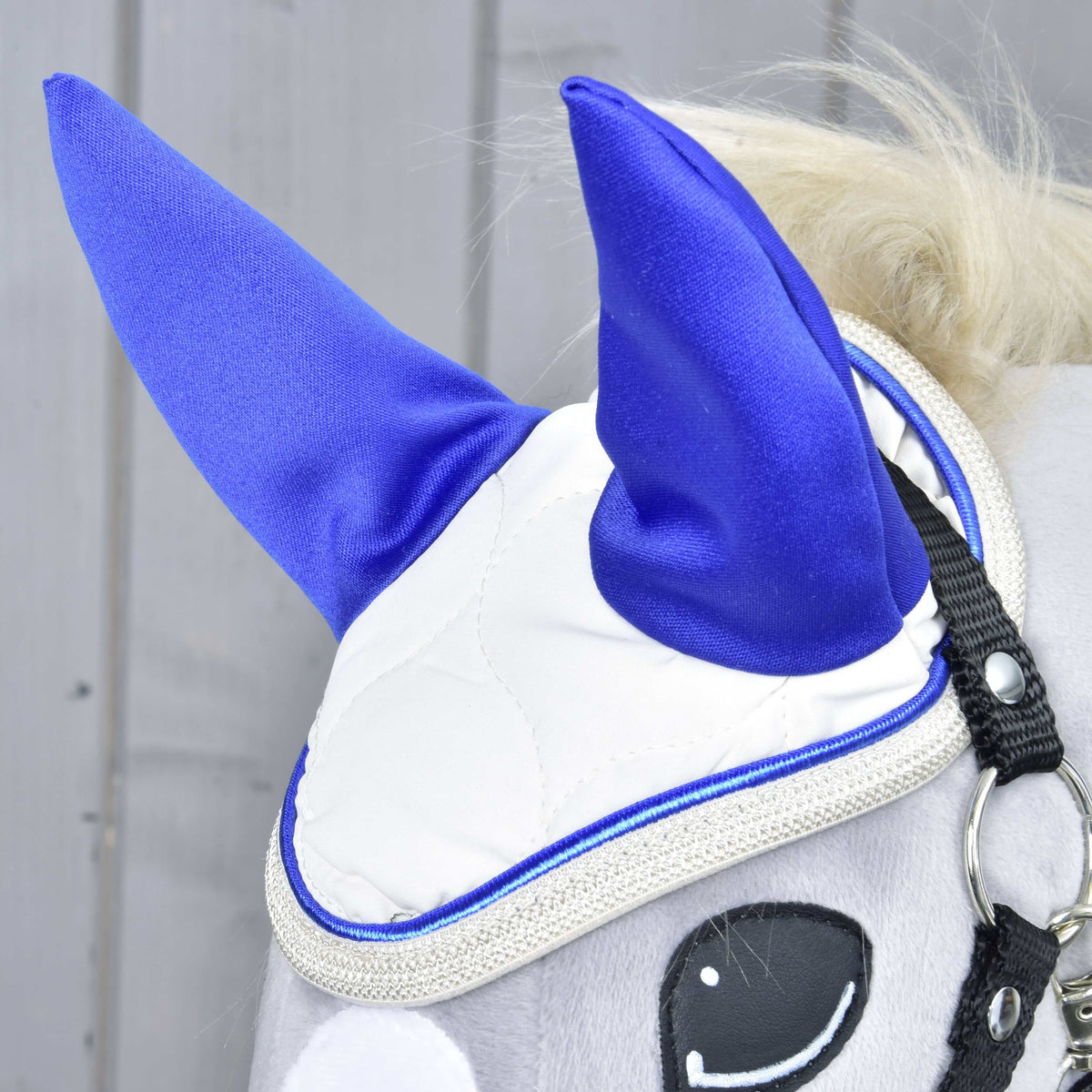 Bližnji posnetek naušnikov Cream Pearl na sivem Hobby Horse konju: kraljevsko modra ušesa, smetanasto prešito blago in bleščeč srebrn rob