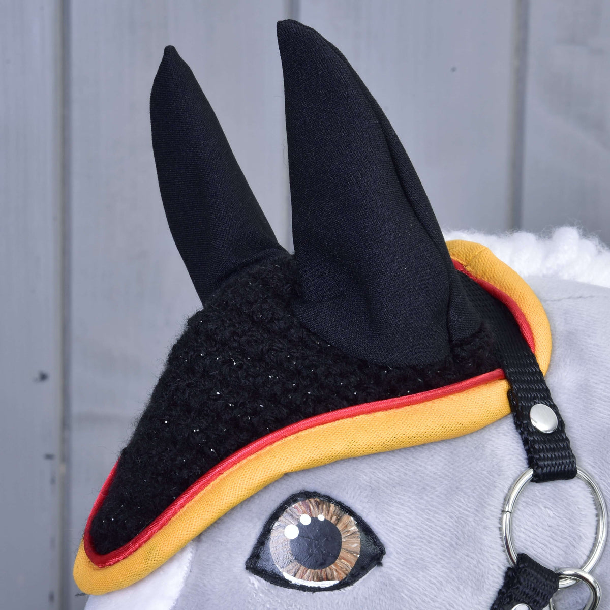 Close-up of the sparkly black crochet, black ears and red and yellow piping of the Flag ear bonnet on a Hobby Horse