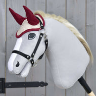 Svetlo siv Hobby Horse konj z blond grivo nosi naušnike Maroon Star in črno oglavko ob sivih lesenih vratih