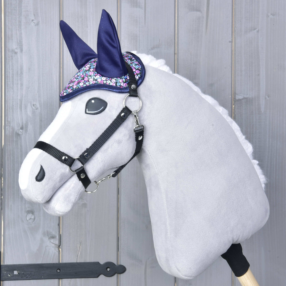Siv Hobby Horse konj s črno oglavko in temno modrimi naušniki z drobnim cvetličnim potiskom čez čelo