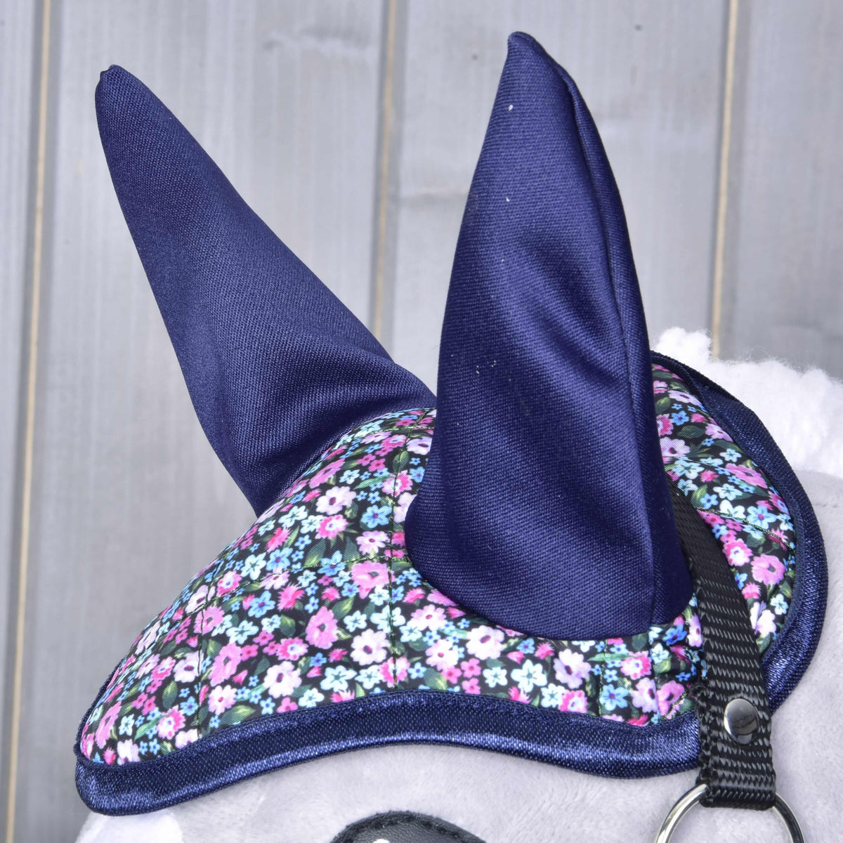 Bližnji posnetek temno modrih ušes in prešitega temena s cvetličnim potiskom ter temno modro obrobo na glavi sivega Hobby Horse konja