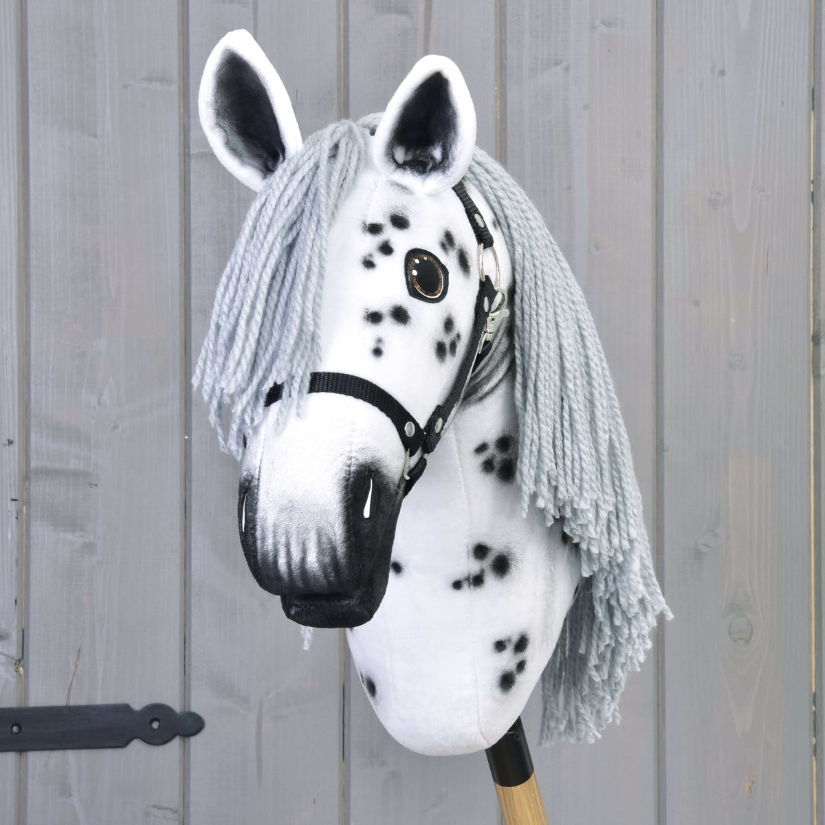 Pogled od spredaj na Hobby Horse konja Chantal s sivim čopom iz preje, belimi ušesi s temno notranjostjo in temno osenčenim gobcem