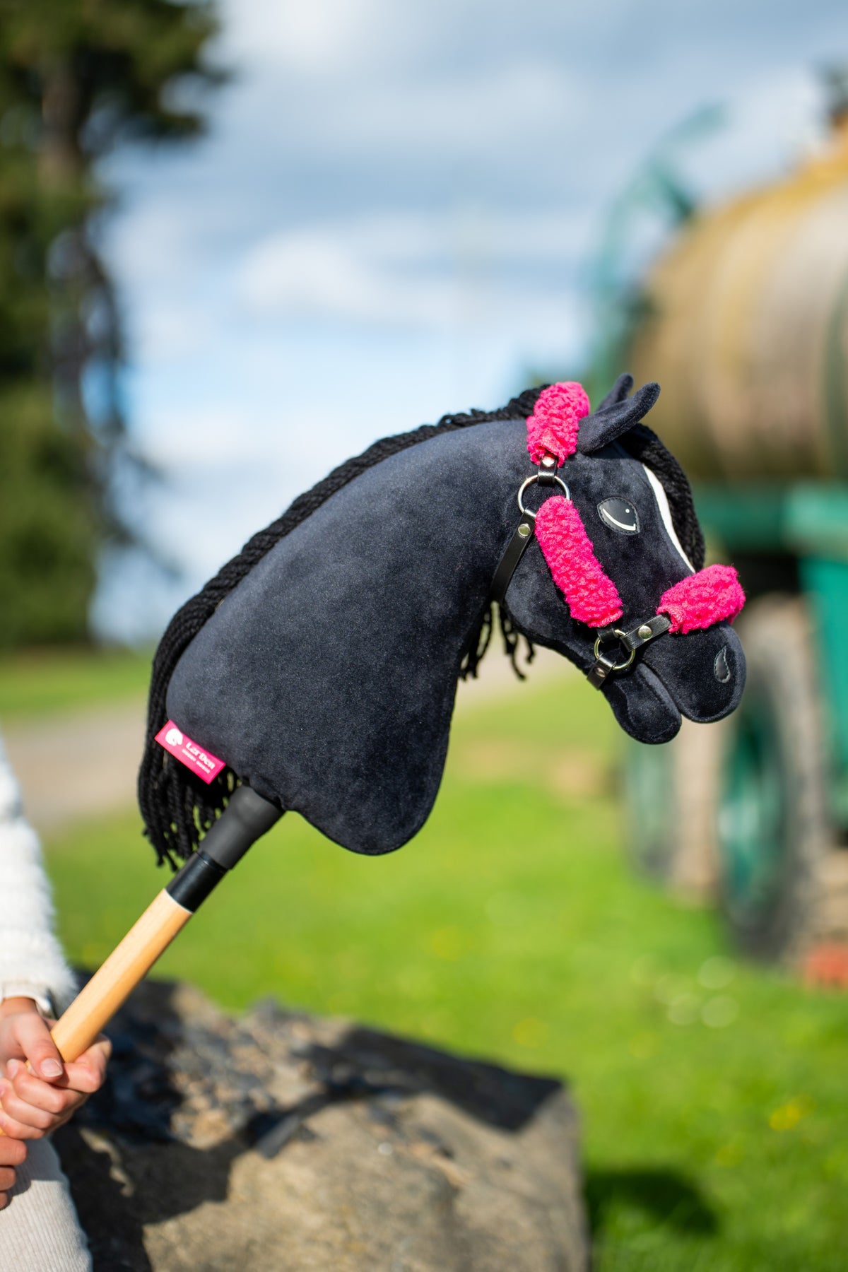 Črn plišast Hobby Horse konj z belo liso in črno grivo iz preje v črni oglavki z roza krznom, dvignjen v zrak na prostem