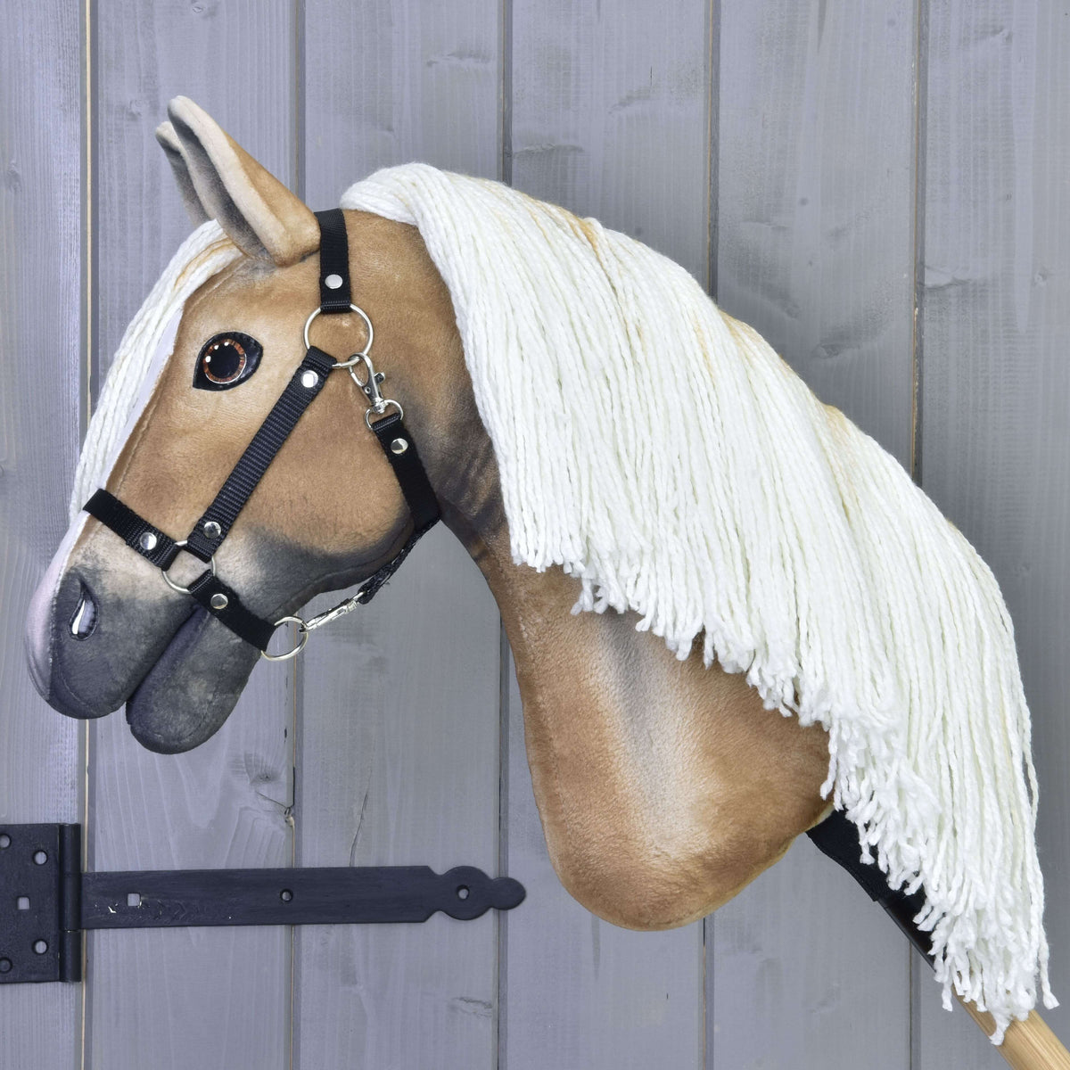 Pogled od strani na zlato rjavega Hobby Horse konja z dolgo kremno grivo iz preje in črno oglavko na leseni palici